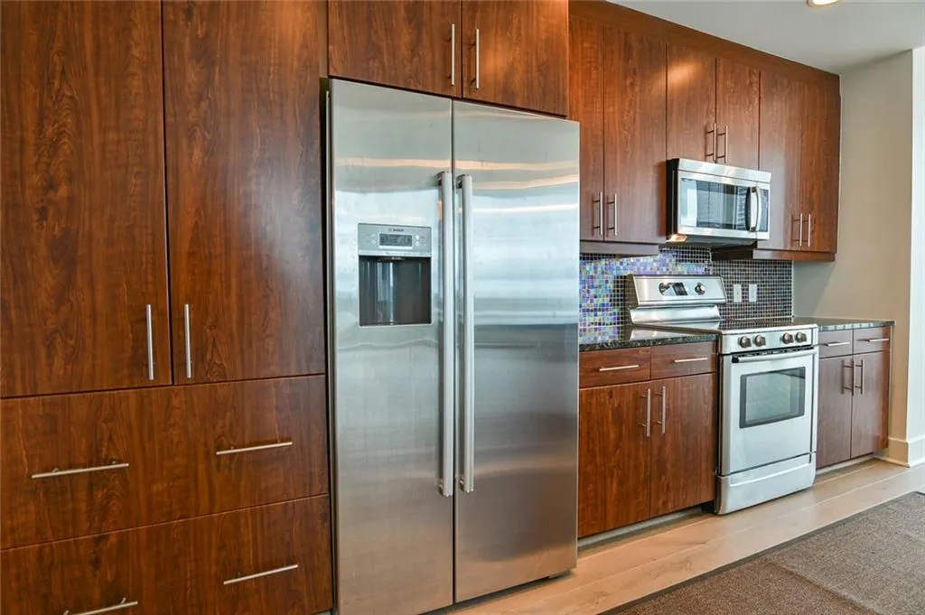 Kitchen with stainless steel appliances, light wood finished floors, decorative backsplash, recessed lighting, and dark stone counters