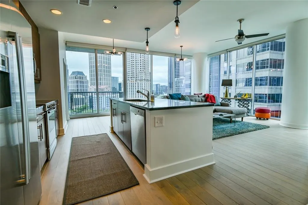 Kitchen featuring appliances with stainless steel finishes, wood-type flooring, a skyline view, dark countertops, and a center island with sink
