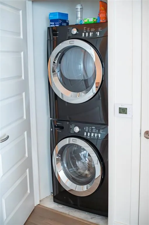 Washroom with stacked washer / dryer and wood finished floors