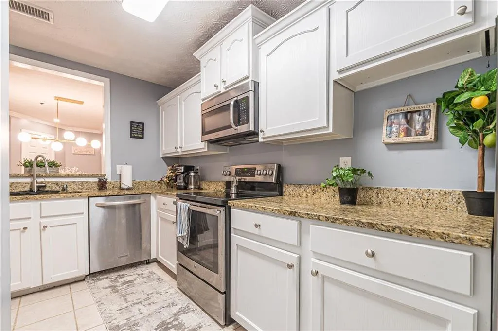 Kitchen with stainless steel appliances, white cabinets, light stone counters, light tile patterned floors, and decorative light fixtures