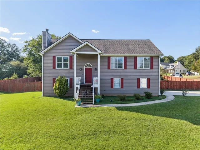 Two-story residence featuring a covered front porch with white railings, a red front door with an arched transom, and gray siding with red shutters