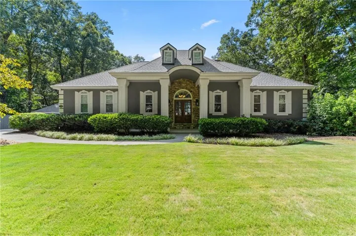 Stucco and stone facade with dormer windows, a double-door entry, and a covered porch supported by columns