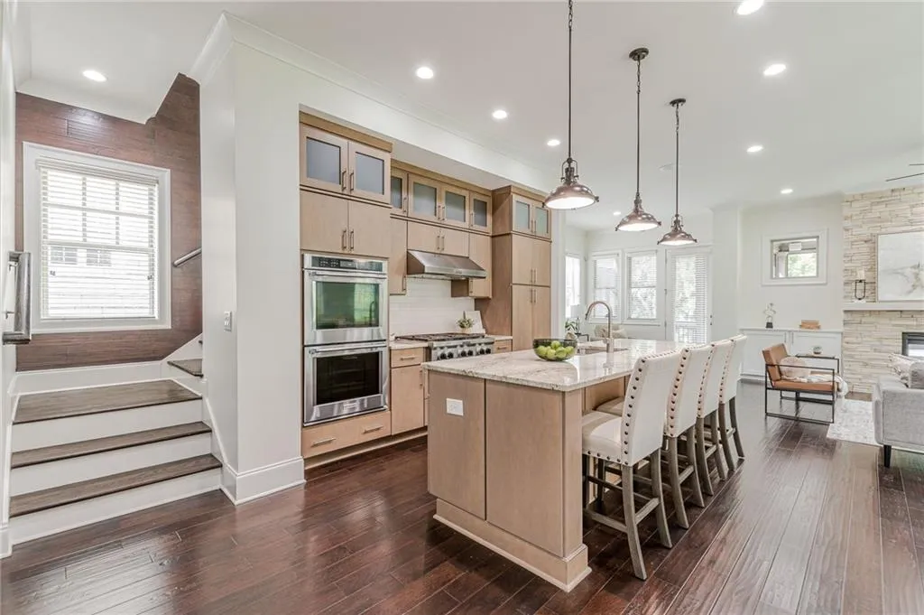 Kitchen featuring dark wood-type flooring, light stone counters, a kitchen island with sink, appliances with stainless steel finishes, and a kitchen breakfast bar