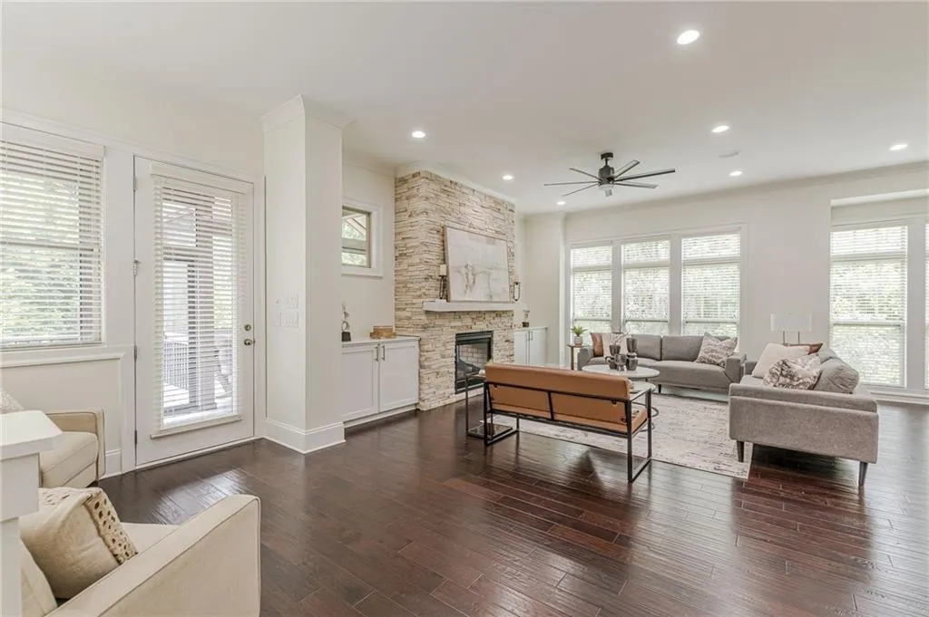 Living room featuring a stone fireplace, dark wood-type flooring, a healthy amount of sunlight, and ceiling fan