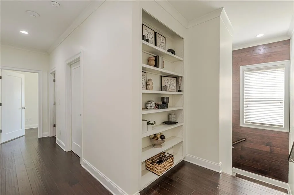 Hallway with dark wood-type flooring, built in shelves, and ornamental molding