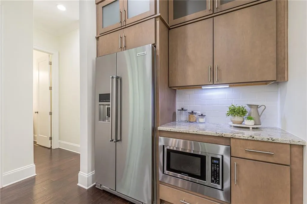 Kitchen featuring decorative backsplash, appliances with stainless steel finishes, dark hardwood / wood-style floors, and light stone counters