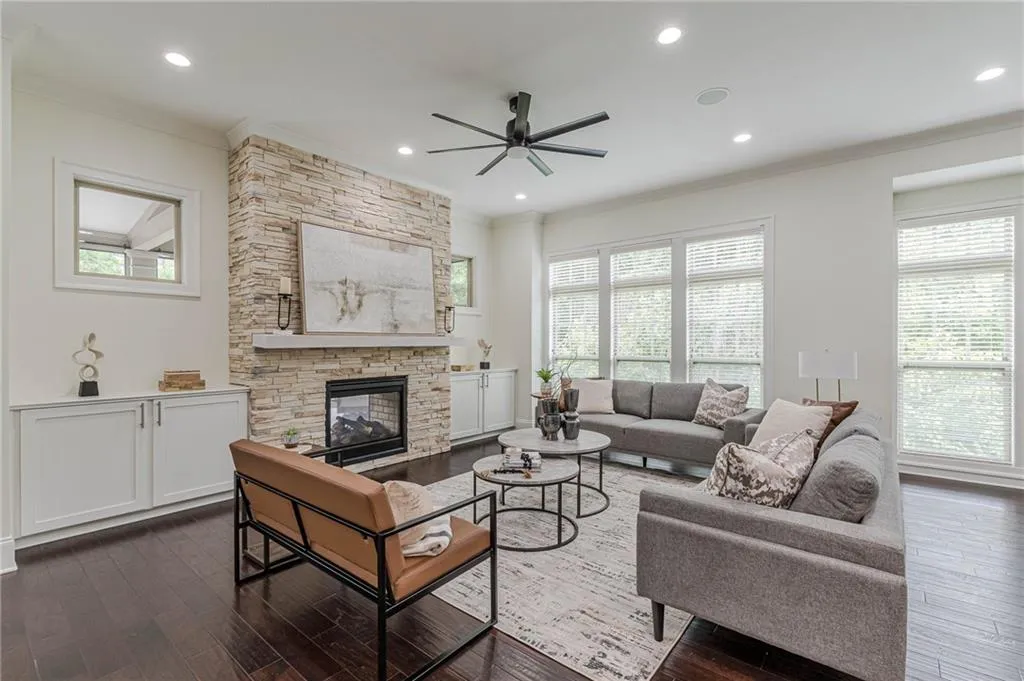 Living room with ornamental molding, a stone fireplace, dark hardwood / wood-style floors, and ceiling fan