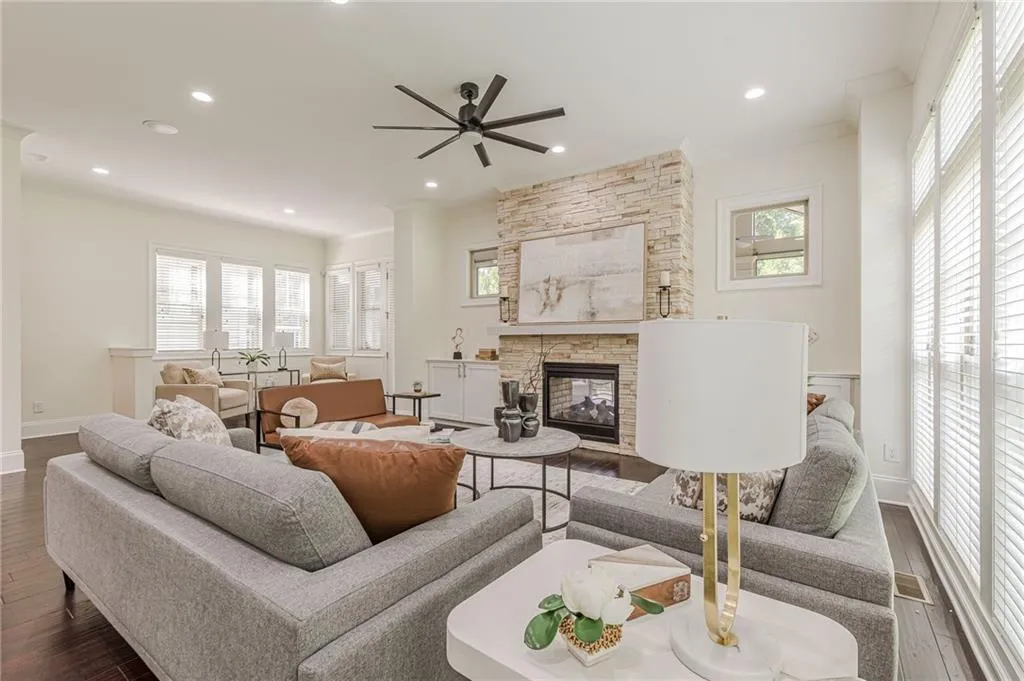 Living room with ornamental molding, dark hardwood / wood-style flooring, a stone fireplace, and ceiling fan