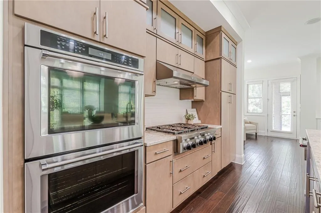 Kitchen featuring dark hardwood / wood-style flooring, appliances with stainless steel finishes, light brown cabinetry, decorative backsplash, and ornamental molding