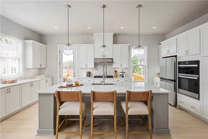 Kitchen featuring light countertops, under cabinet range hood, a breakfast bar area, multiple ovens, and freestanding refrigerator