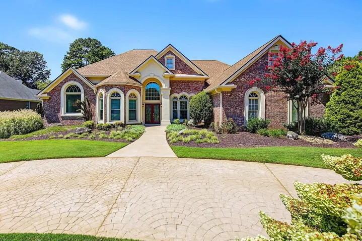 Elegant brick residence featuring a curved driveway with decorative paver detailing, arched entryways with transom windows, and professionally landscaped grounds with mature plantings and manicured lawn