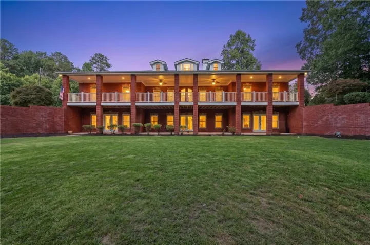 Red brick exterior featuring a multi-level covered porch with white railings, dormer windows, and a manicured lawn