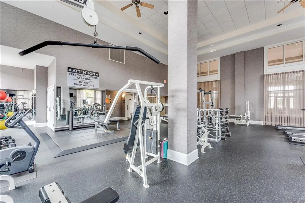 Gym with baseboards, a paneled ceiling, ceiling fan, and a towering ceiling