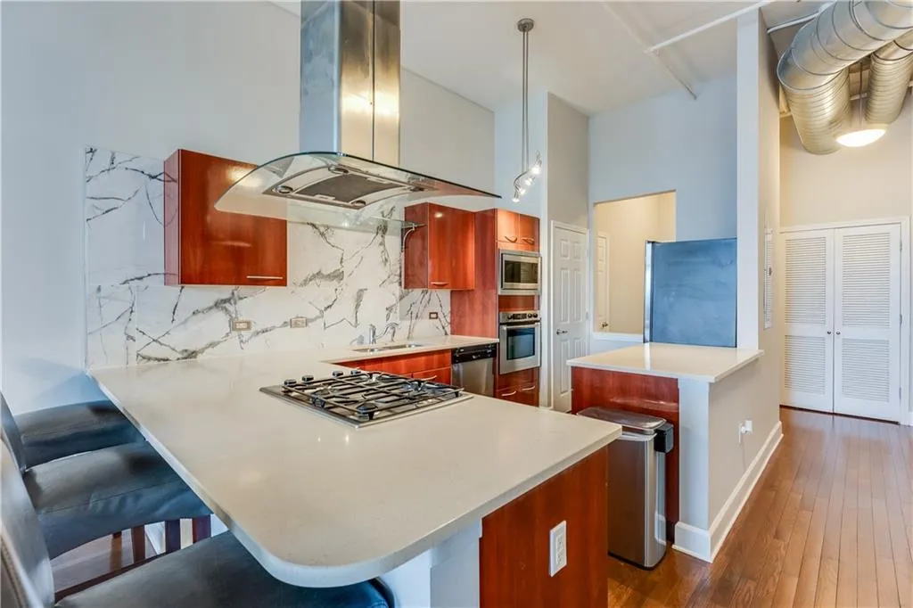 Kitchen with island exhaust hood, dark wood-style floors, appliances with stainless steel finishes, a peninsula, and decorative backsplash