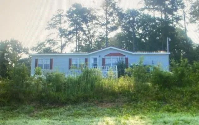 Light-colored siding with red window shutters and a front deck with white lattice details