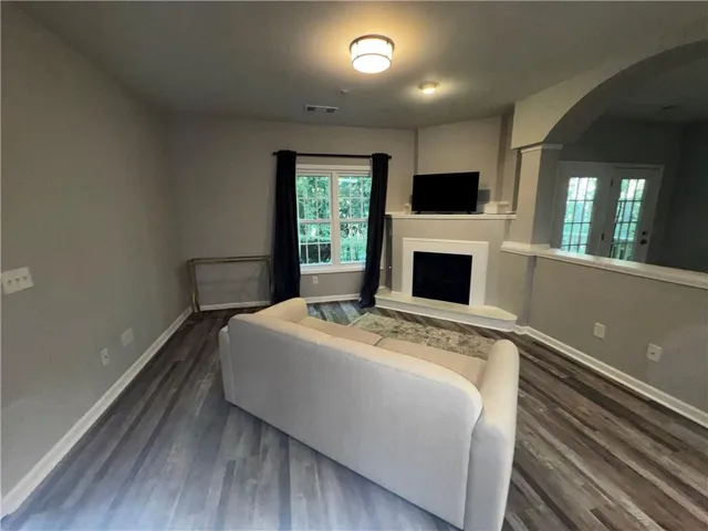 Living area with wood-finish flooring, a corner fireplace, and an arched opening to a separate space with double glass doors