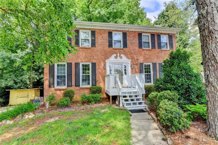 Brick two-story colonial-style residence featuring black louvered shutters, a white columned portico, and a multi-level white wooden staircase