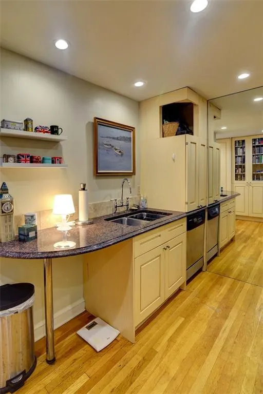 Kitchen with a sink, light wood-style floors, stainless steel dishwasher, dark stone counters, and recessed lighting
