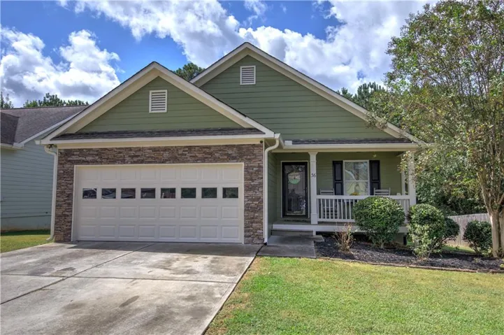 Front exterior featuring a covered porch with white railings, a two-car garage with window inserts, stone accent siding, and a green façade