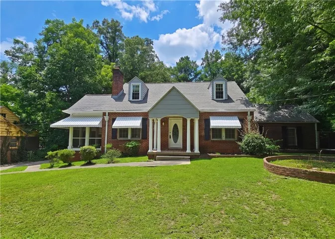 Brick exterior home featuring a columned front entrance, two front dormer windows, and a side-gabled roofline