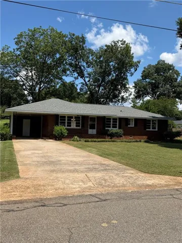 Brick exterior, gray shingle roof, attached carport, concrete driveway, and front lawn