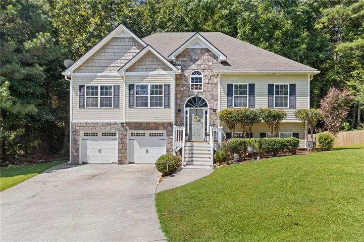 Two-story residence featuring stone and siding facade, dual garage doors, a curved concrete driveway, and established landscaping