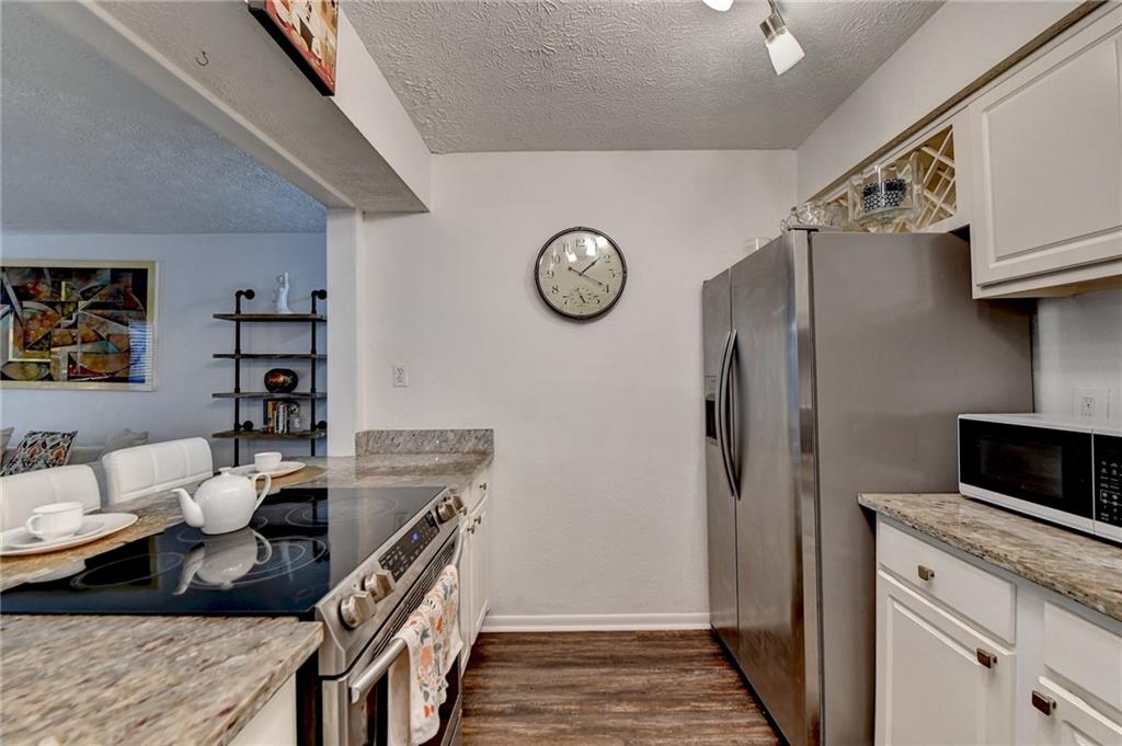 Kitchen with dark wood-type flooring, white cabinets, granite countertops,  and appliances with stainless steel finishes