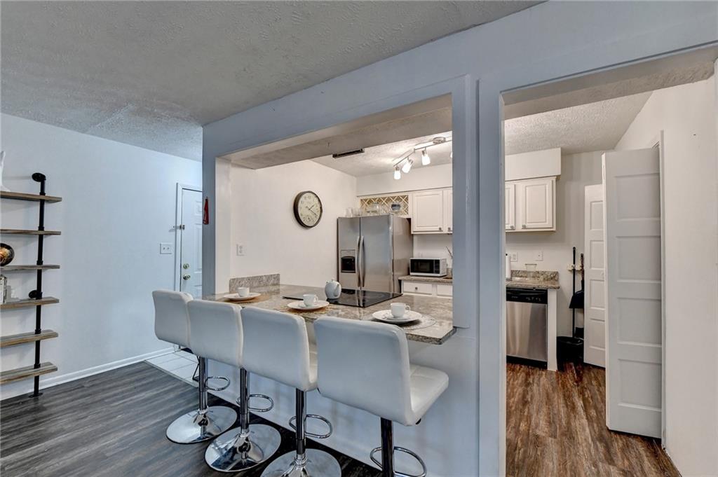 Kitchen with dark hardwood / wood-style flooring, stainless steel appliances, white cabinetry and a kitchen breakfast bar