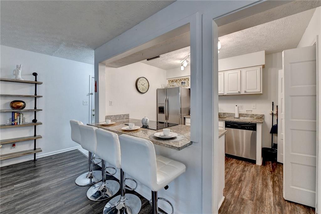 Kitchen featuring a textured ceiling, light stone countertops, white cabinetry, dark hardwood / wood-style flooring, and stainless steel appliances
