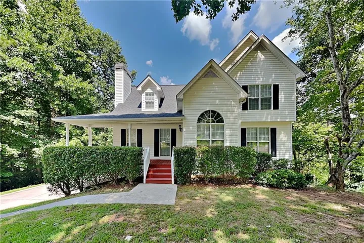 White siding exterior featuring a gable roof, covered porch, dormer windows, and a prominent arched window