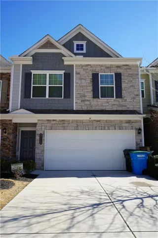 View of front of property featuring an attached garage, stone siding, and driveway