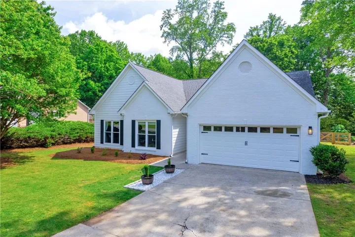 White brick exterior with dark shutters, attached garage with decorative hardware, and a paved driveway
