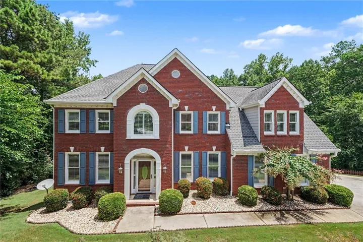 Brick facade residence featuring a prominent arched entry, multiple gabled rooflines, and decorative blue shutters