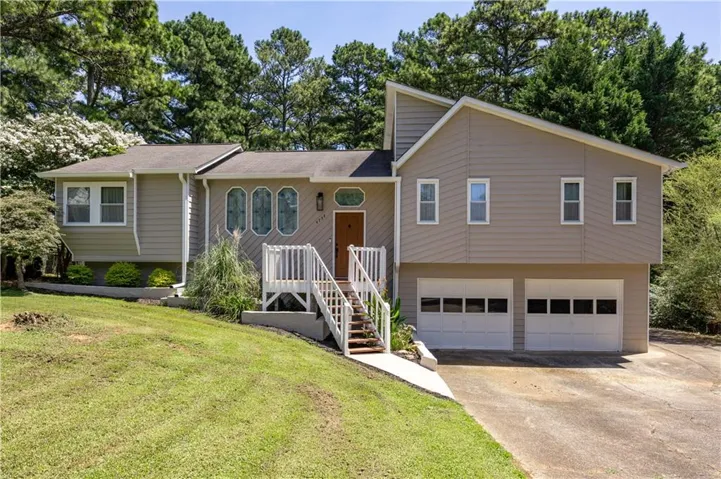 Contemporary split-level residence featuring a neutral siding exterior, two-car garage, white railing entry stairs, and established landscaping