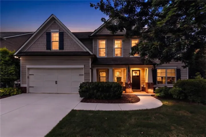 Traditional-style home featuring a two-car garage, established landscaping, a concrete driveway, and a welcoming front porch with brick accents