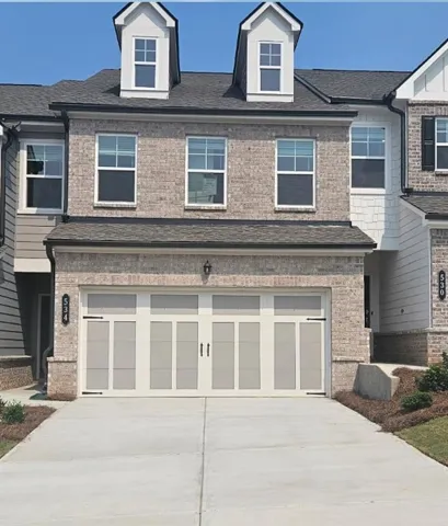 Brick facade with two prominent dormer windows, a two-car garage with decorative hardware, and an asphalt shingle roof