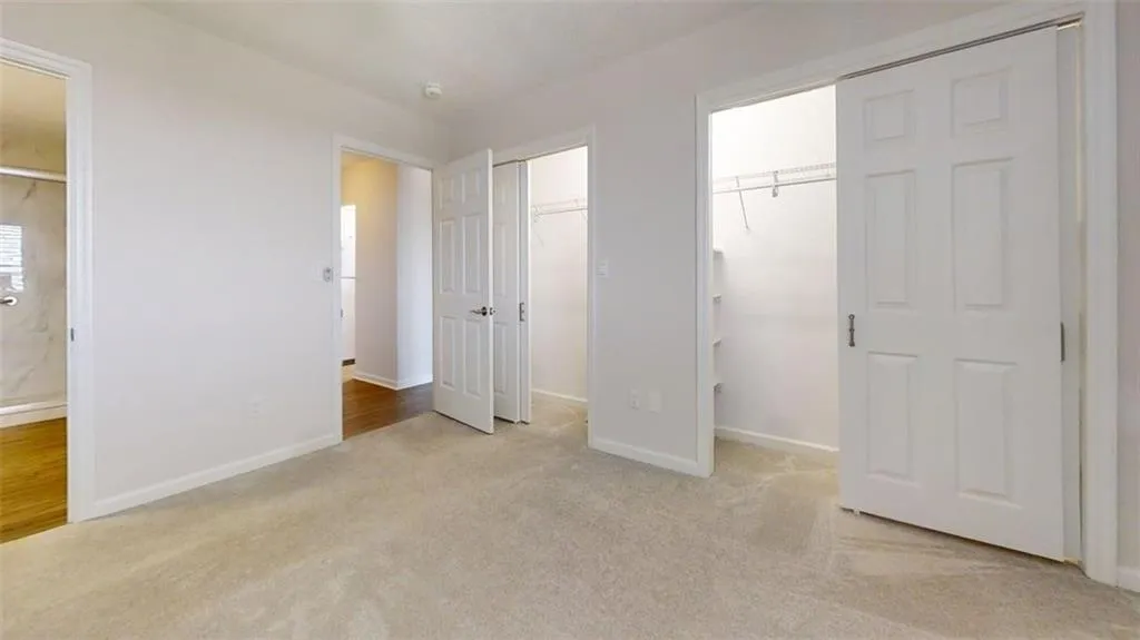 Unfurnished bedroom featuring light carpet, connected bathroom, and multiple closets