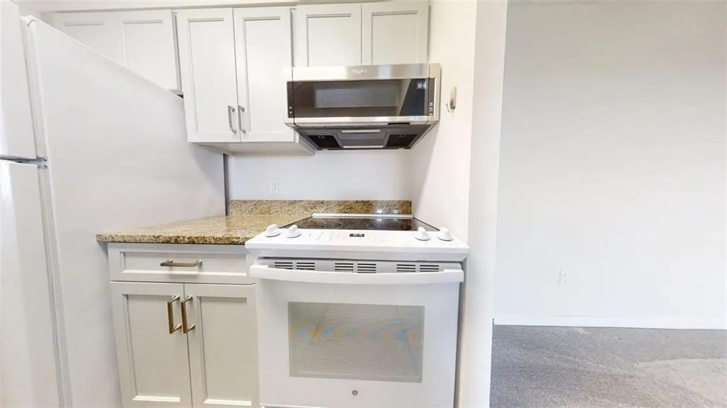 Kitchen with white appliances, white cabinetry, light stone counters, and carpet