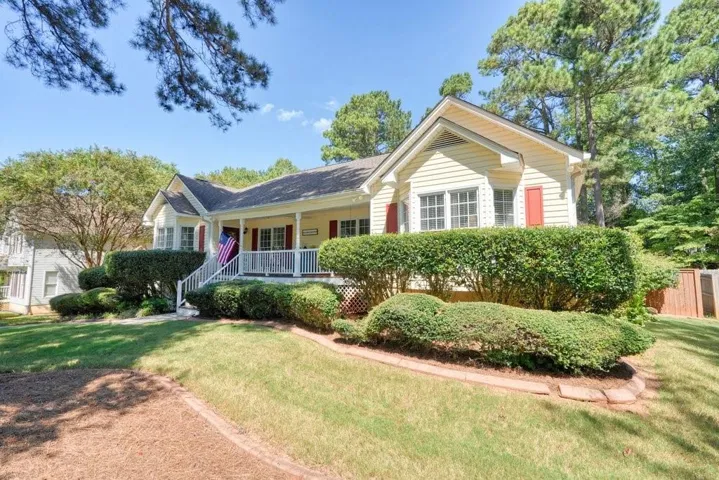 Light yellow siding exterior with red window shutters, a covered front porch with white railings, and a gabled roof