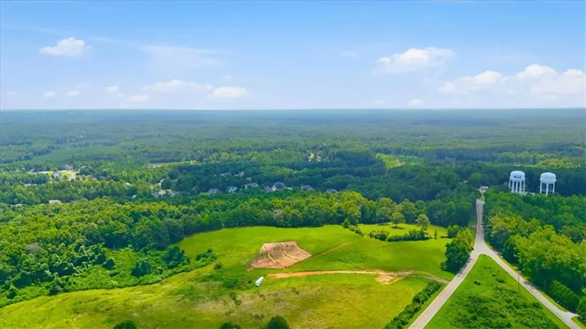 Expansive green landscape featuring a distant residential area, dense tree cover, and paved roadway access