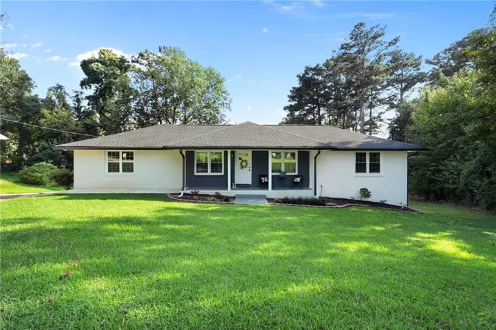 Single-story residence featuring white brick exterior with dark accent siding, a dark shingle roof, and a front porch
