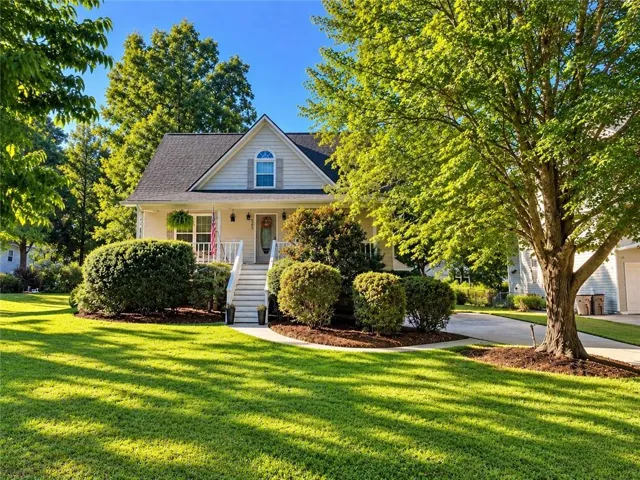 Gabled roofline with dormer window, covered front porch, white railings, concrete steps, and a paved driveway