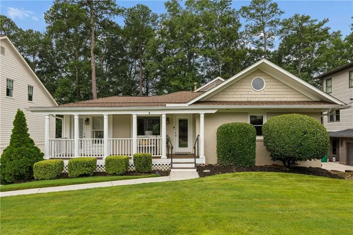 Single-story residence featuring a covered front porch with white railings, a front-facing gable with shingle siding and a round window, and a light-colored brick exterior