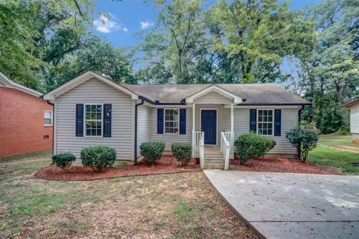 Light-colored siding exterior with dark shutters, covered front entry, concrete driveway, and mature landscaping