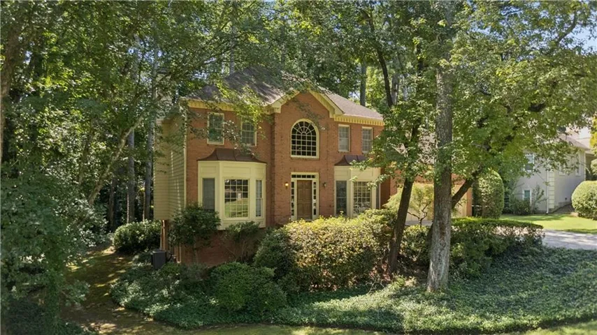 Brick exterior with a prominent arched window, bay window with a copper-tone roof, and mature landscaping