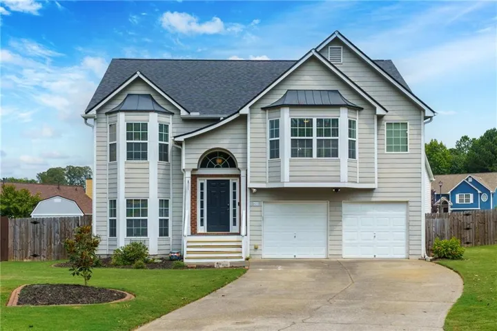 Two-story residence featuring light-toned siding, a dark-toned roof, and bay windows