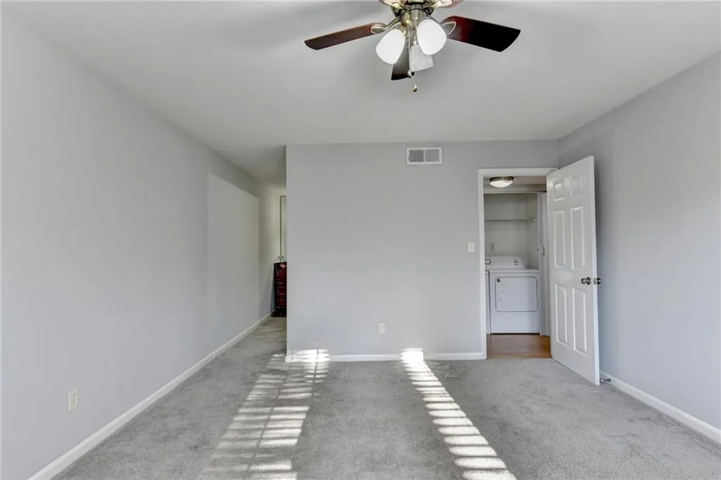 Unfurnished bedroom with washer / dryer, light colored carpet, and a ceiling fan