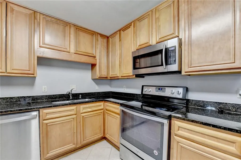 Kitchen with stainless steel appliances, dark stone counters, light wood finish cabinets, and light tile patterned floors
