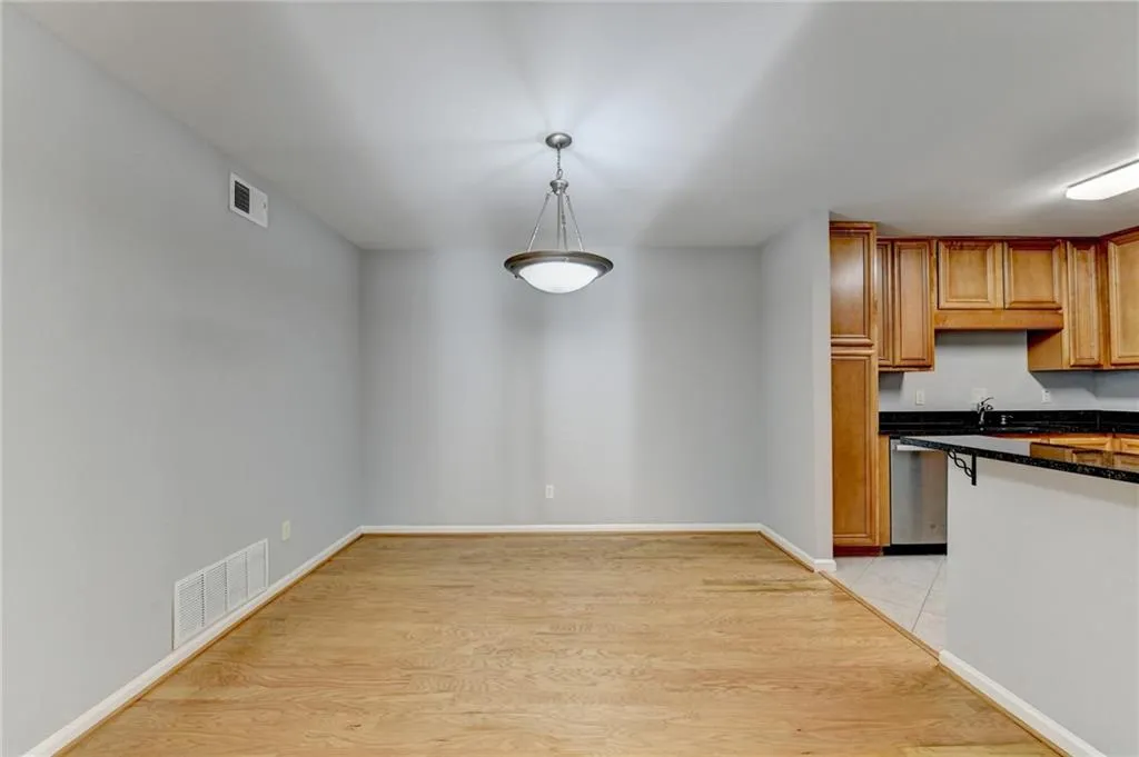 Kitchen with light wood-type flooring, wood finish cabinetry, dark stone countertops, decorative light fixtures, and stainless steel dishwasher