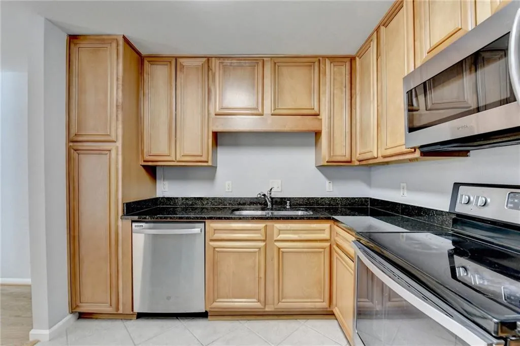 Kitchen with stainless steel appliances, light wood finish cabinetry, dark stone counters, and light tile patterned floors